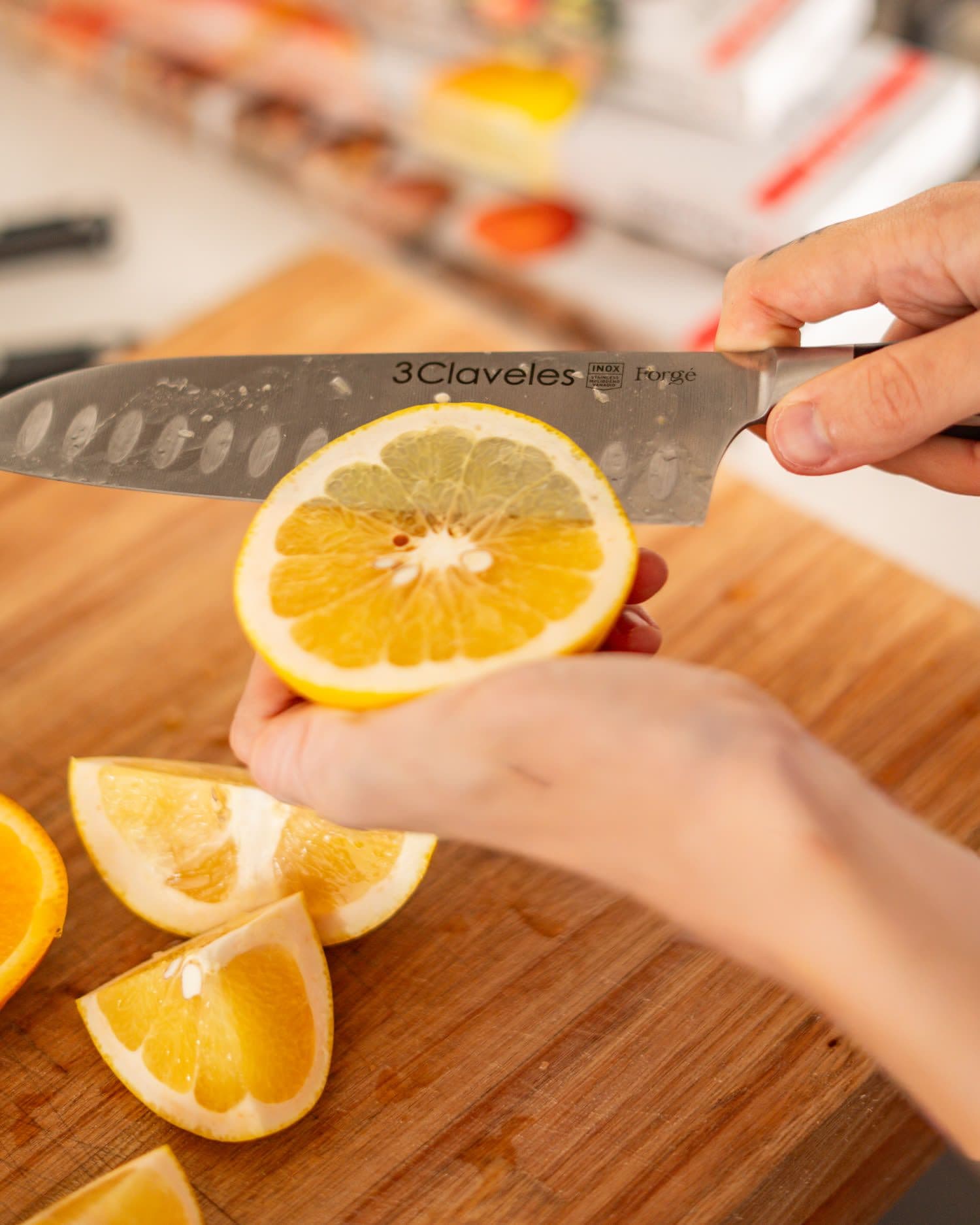 Las manos de Delfina sostienen media naranja recién cortada junto a un cuchillo 3 Claveles, sobre una tabla de madera con los gajos alrededor.